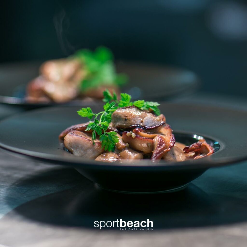 Plat dans une assiette noire avec morceaux de viande garnis de feuilles vertes, sur une table sombre.