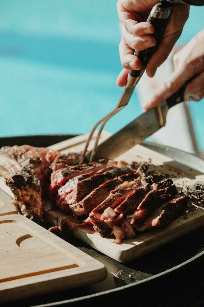 Main découpant un steak grillé en tranches sur une planche en bois.