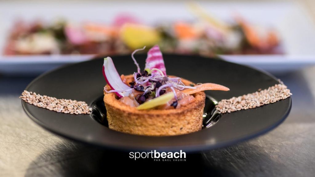 Plat gastronomique présenté dans une assiette noire, garni de légumes finement coupés et de graines.