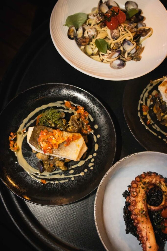 Assiettes de plats cuisinés variés comprenant pâtes aux fruits de mer, filet de poisson et poulpe.